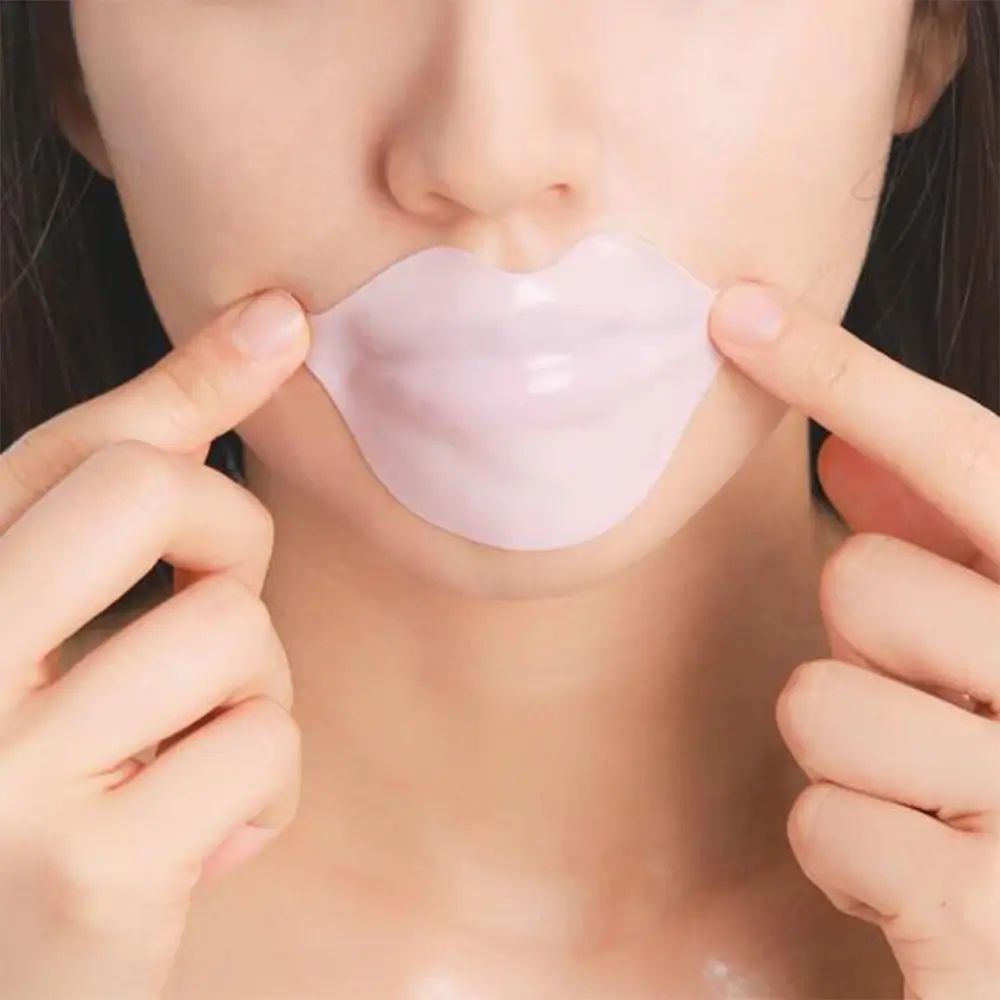 Hydrogel-Lippenmaske auf Lippen. Helle Haut, Hände halten Maske. Rosa Lippenmaske in Lippenform.