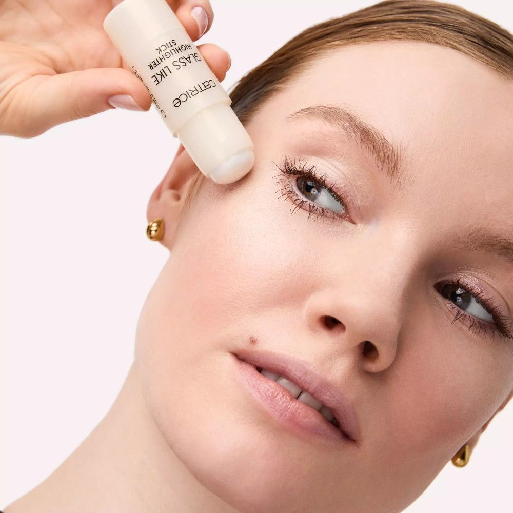 Frauengesicht, Highlighter-Stick wird aufgetragen. Aufschrift: Catrice, GLASS LIKE HIGHLIGHTER STICK.