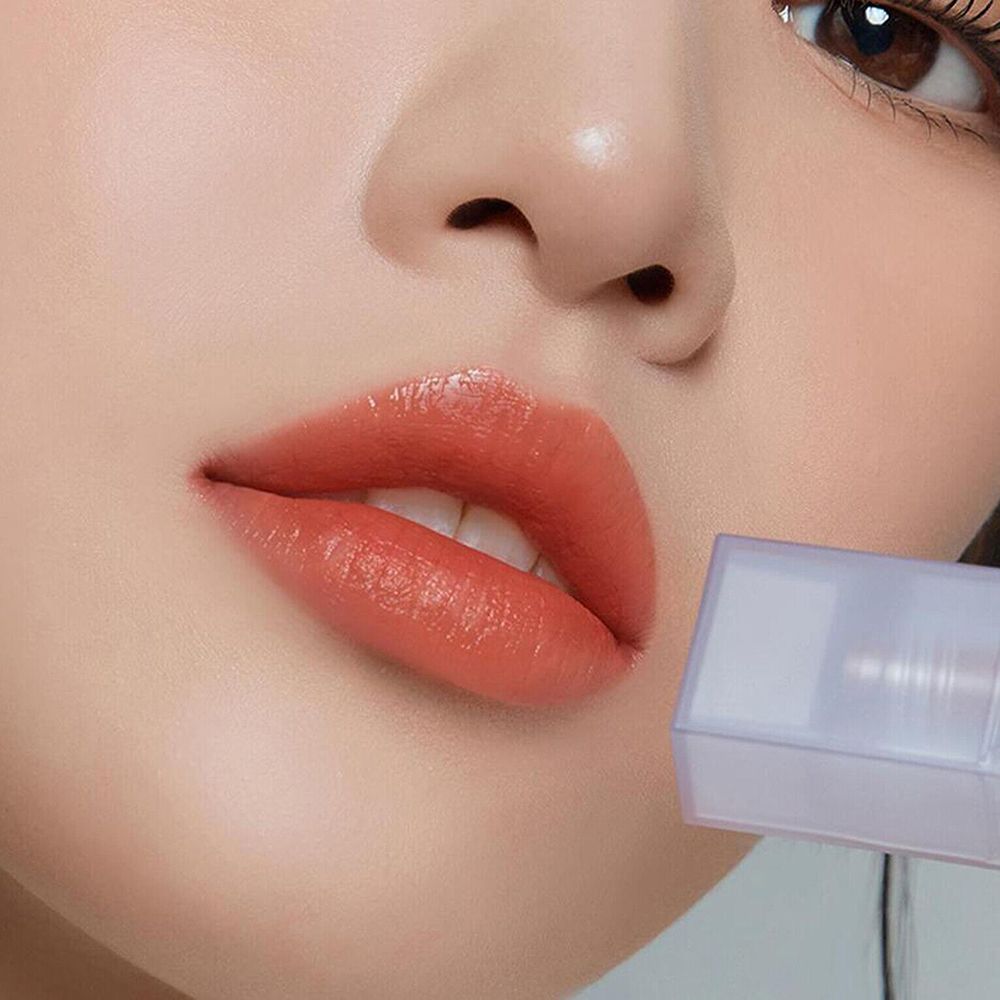 Nahaufnahme von Lippen mit aufgetragenem Lipgloss. Farbe: Apricot. Der Flakon ist teilweise sichtbar.