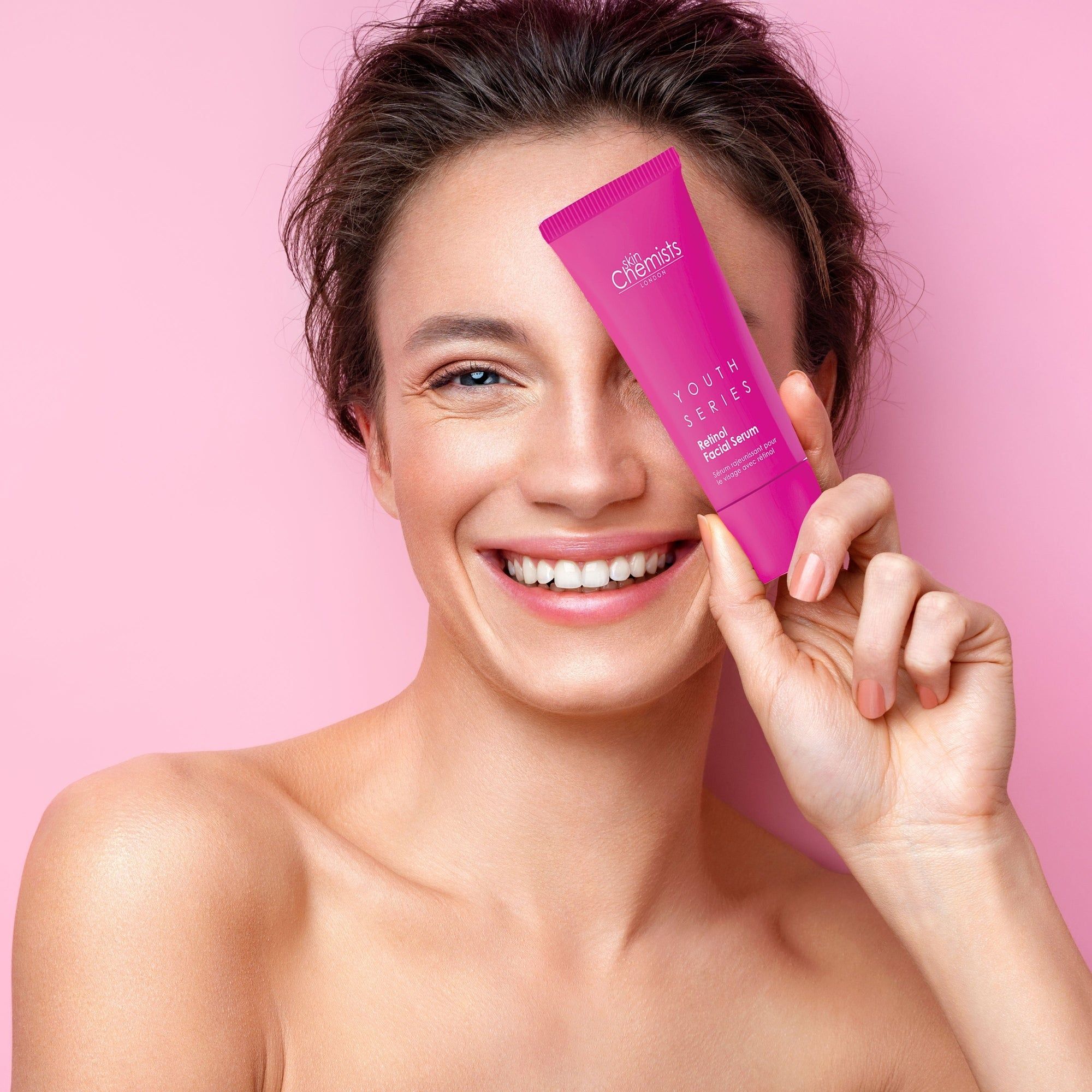 Frau hält eine rosa Tube vor ihr Auge. Auf der Tube steht "skinChemists" und "YOUTH SERIES Retinol Facial Serum".