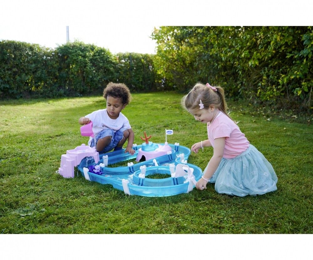 Zwei Kinder spielen mit einem blau-rosa Wasserspielzeug im Garten. Ein Kind gießt Wasser mit einem rosa Becher hinein.