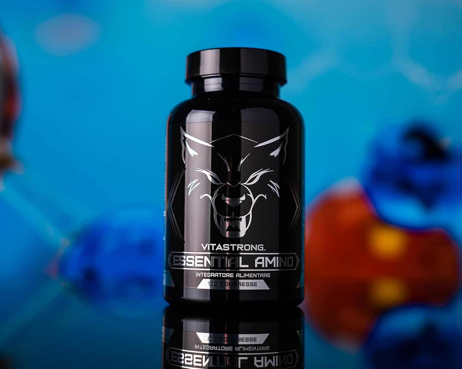 Schwarze Flasche Vitastrong Essential Amino, Tabletten darunter. Aufschrift und Wolf Logo. Blauer Hintergrund.