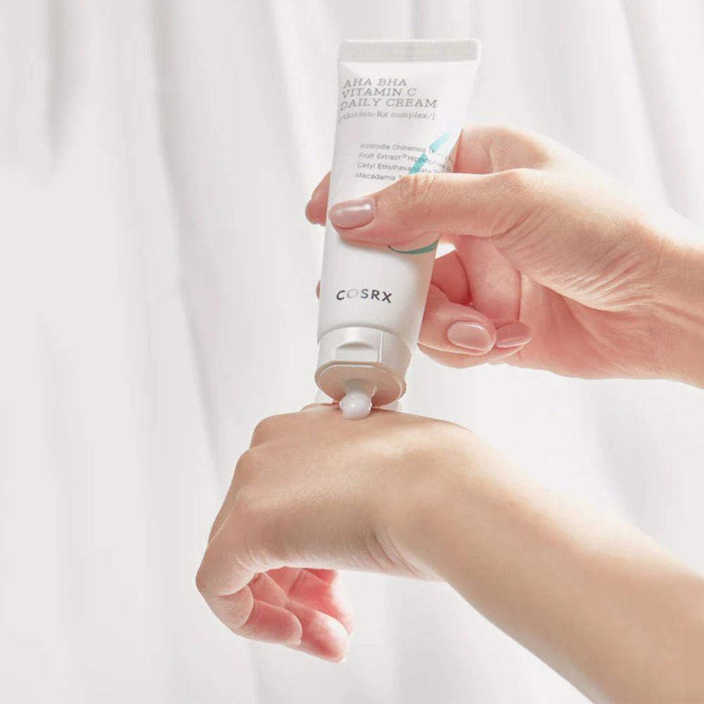 Hände halten eine Tube AHA BHA Vitamin C Daily Cream. Creme wird auf die Hand gedrückt.