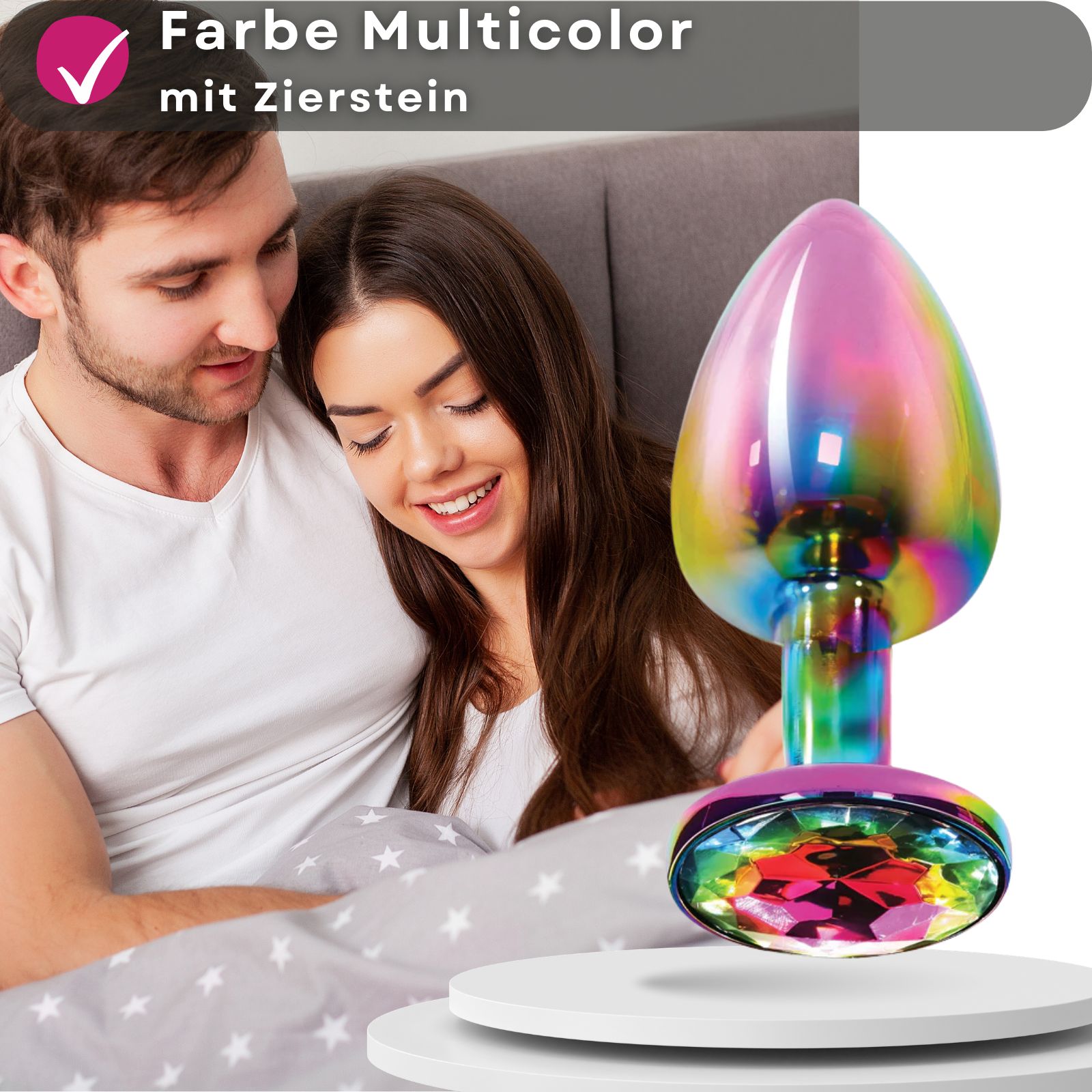 Analplug, mehrfarbig, aus Metall, mit Zierstein. Paar im Hintergrund. Produkt auf Podest.