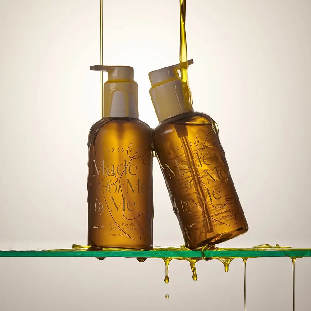 Zwei braune Flaschen mit Ölfluss. Aufschrift: AXIS-Y, Made for Me by Me, Biome Resetting Moringa Cleansing Oil.
