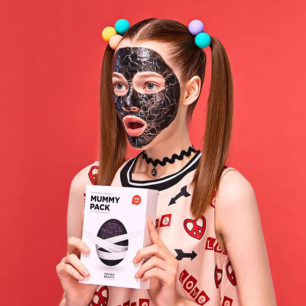 Person mit Gesichtsmaske und einer weißen Box mit Produktaufdruck. Aufdruck: MUMMY PACK.