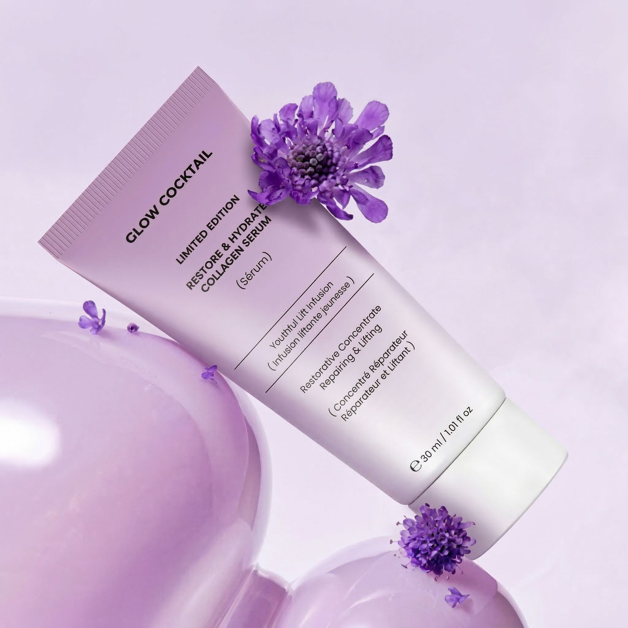 Eine hellviolette Tube mit "Glow Cocktail Restore & Hydrate Collagen Serum" Aufschrift, mit lila Blüten und Blasen.