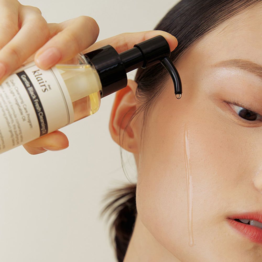 Eine Hand hält eine Flasche Gentle Black Fresh Cleansing Oil. Öl wird auf die Haut aufgetragen.