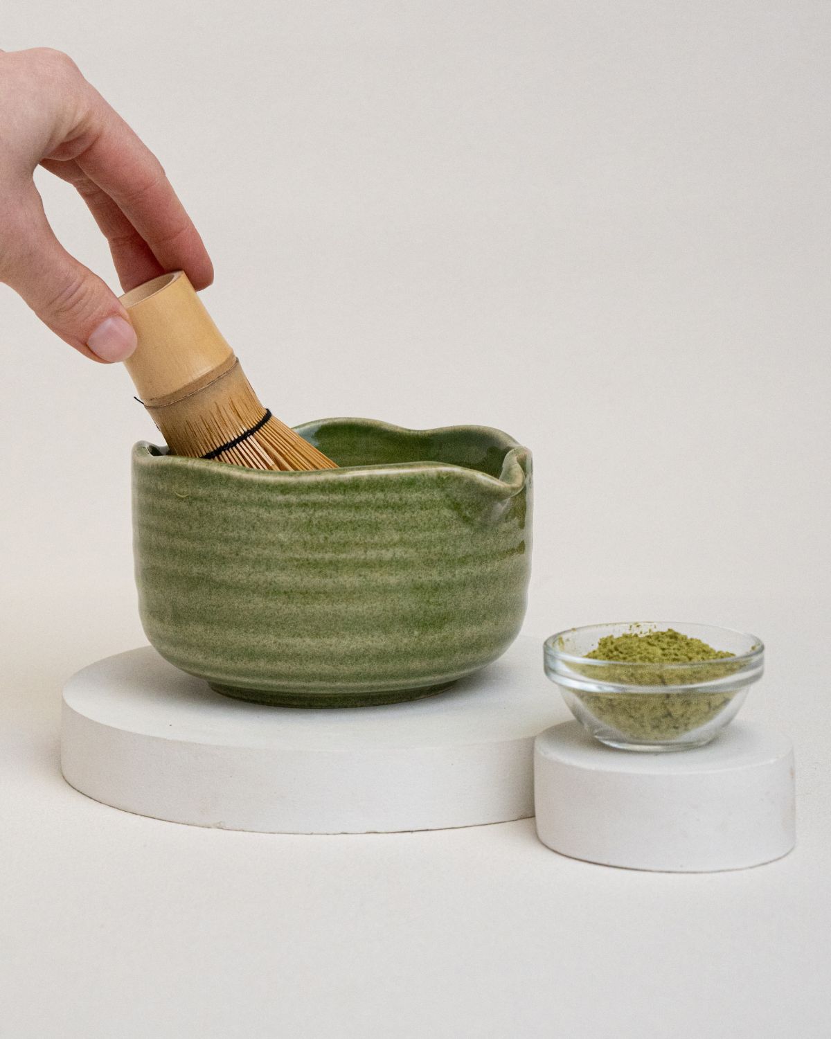Grüne Keramikschale, Matcha-Pulver und Bambusbesen. Eine Hand hält den Besen.