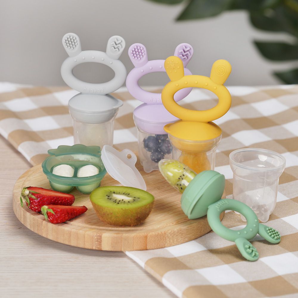 Fruchtsauger und Eiswürfelform auf einem Holzbrett. Dazu Erdbeeren, Kiwi und ein Glas.