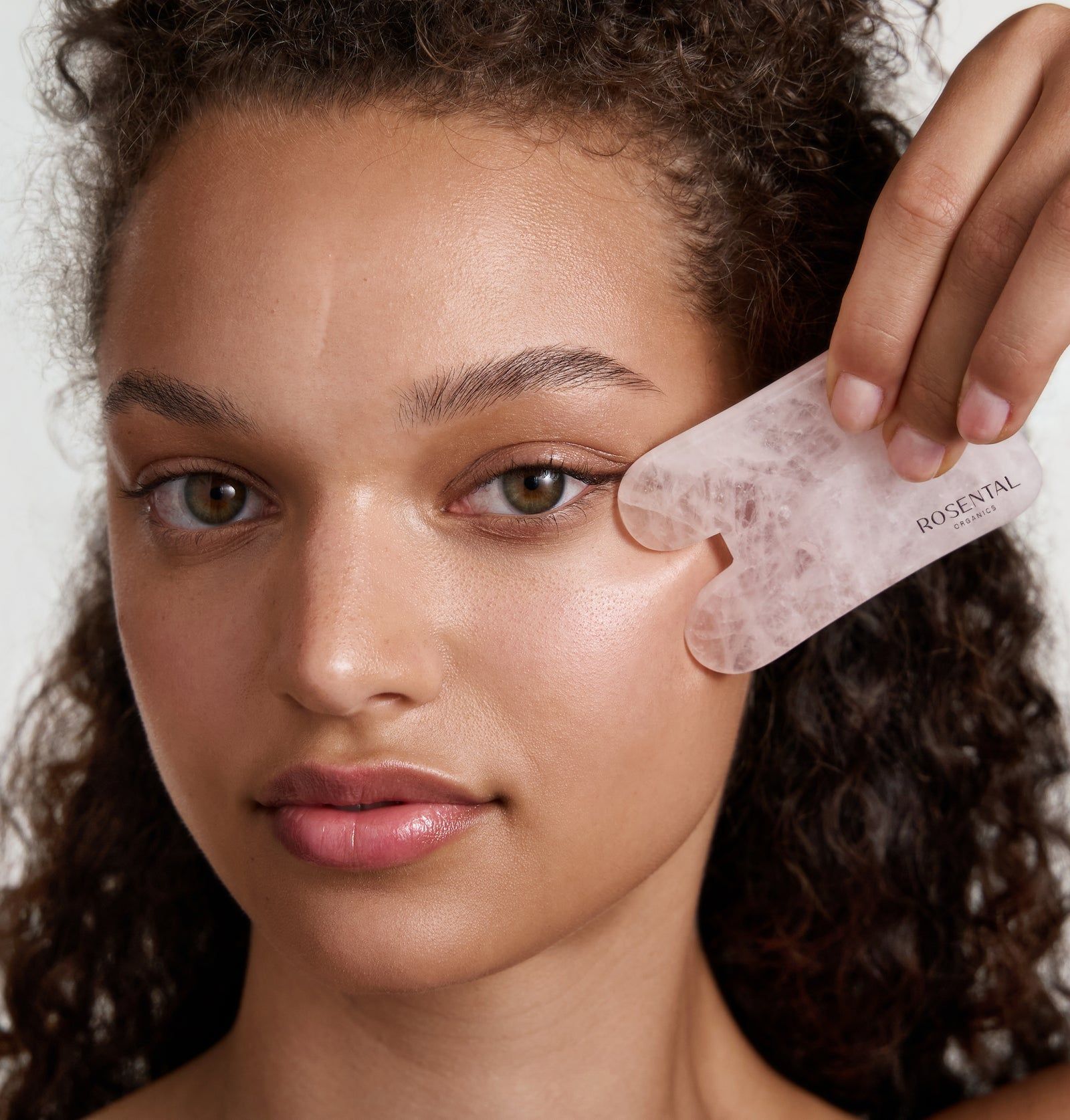Rosental Organics Gua Sha aus Rosenquarz, in Anwendung. Rosa Stein, abgerundete Form mit zwei Aussparungen. Auf Gesicht platziert.