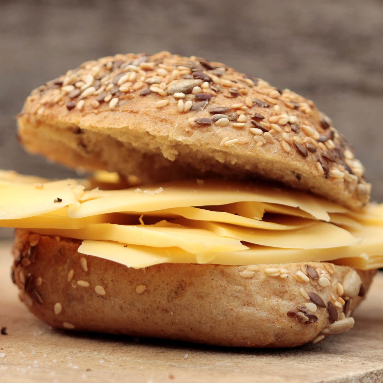 Halbiertes Brötchen mit Käsescheiben. Brötchenhälfte mit Körnern und Samen, belegt mit Käsescheiben. Hintergrund unscharf.