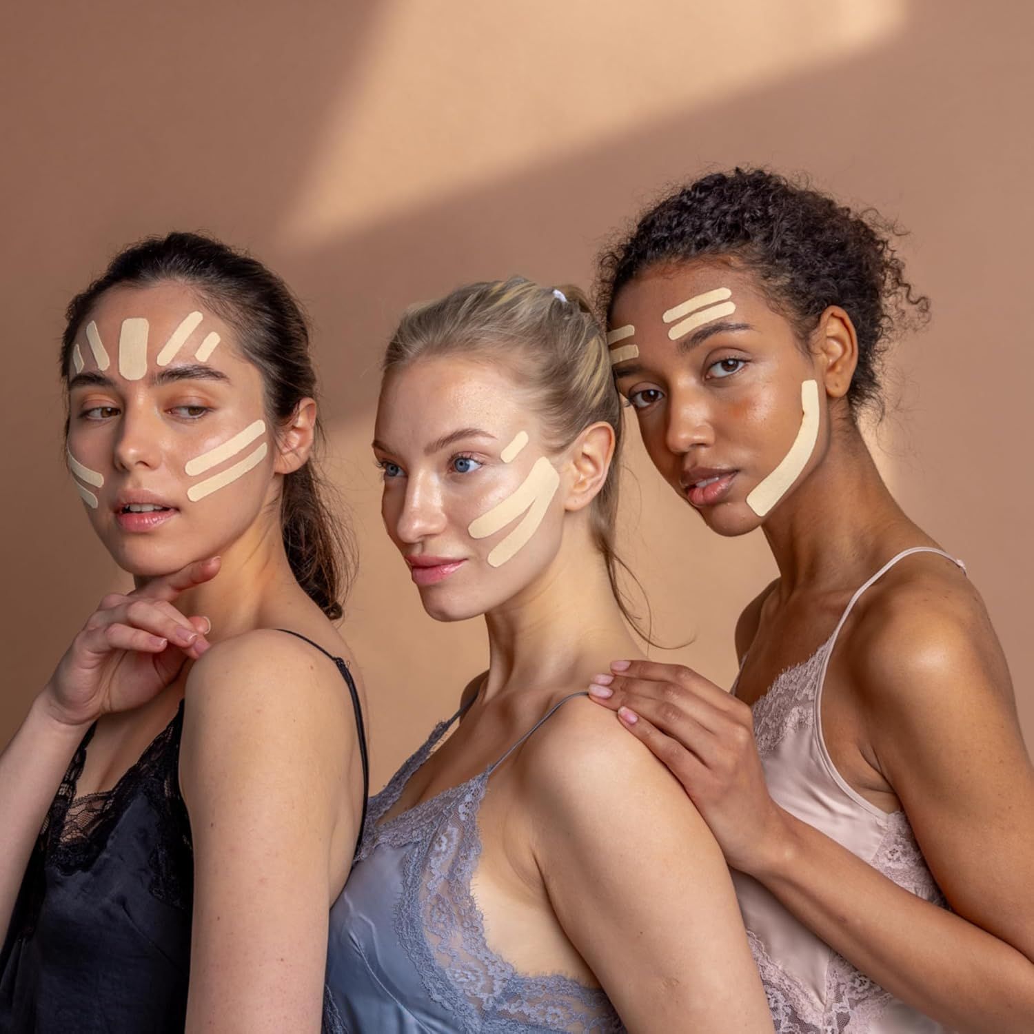 Drei Frauen mit Tape-Streifen im Gesicht. Verschiedene Hauttöne. Tragen Tops.