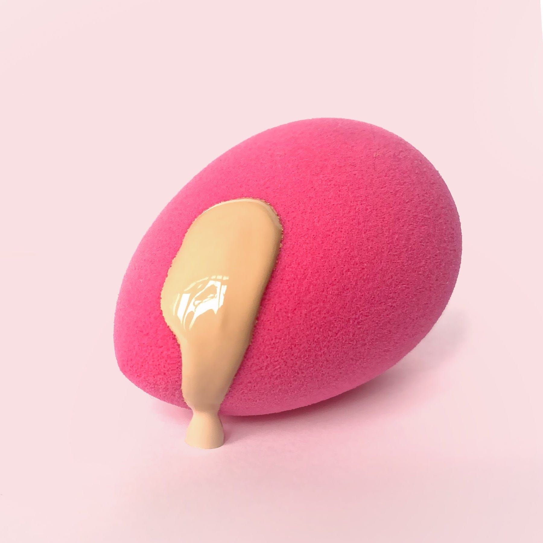 Eine pinke Make-up-Schminkquaste mit flüssiger Foundation, die heruntertropft.