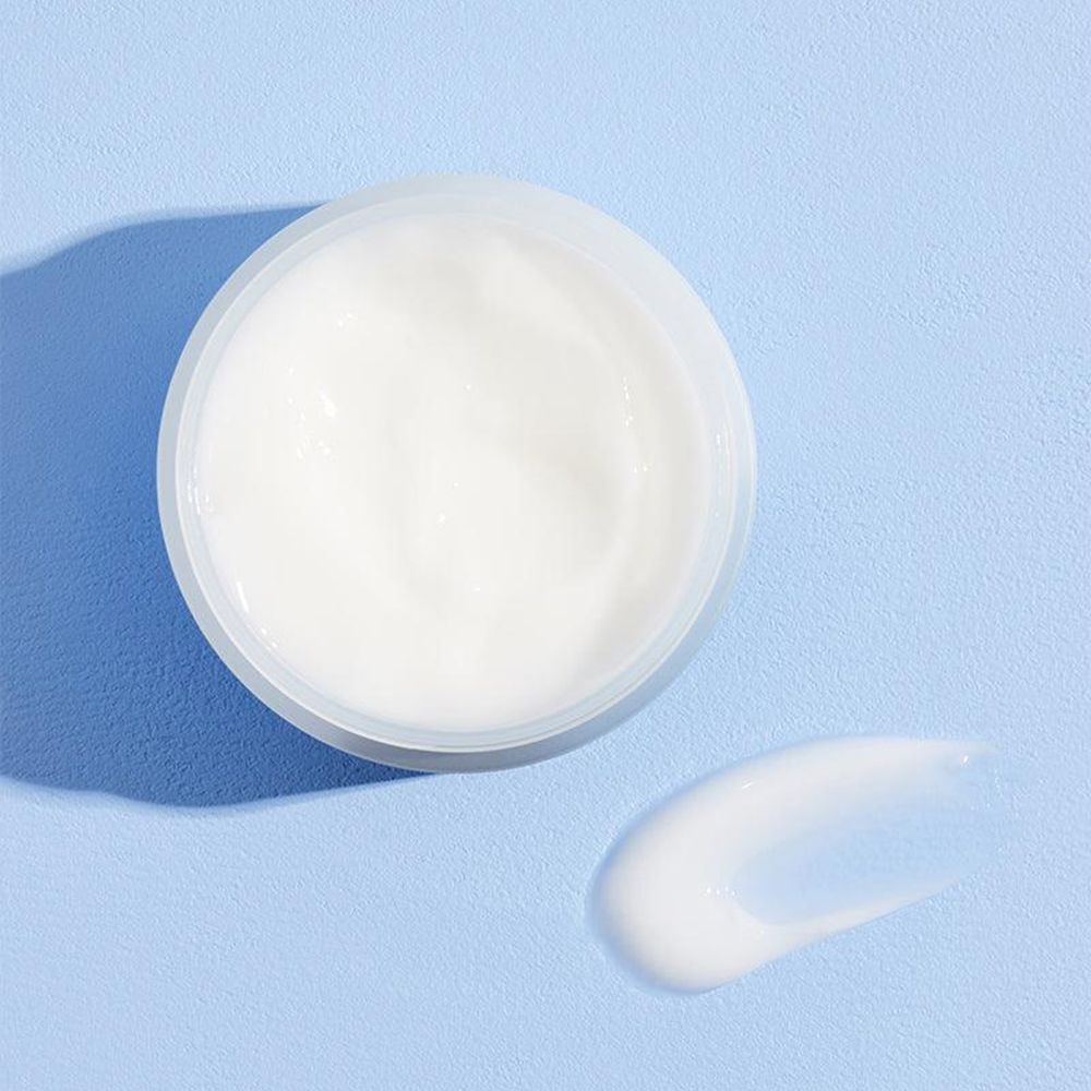 Ein offener weißer Tiegel mit einer weißen Creme und einem Cremeschwung daneben auf blauem Hintergrund.