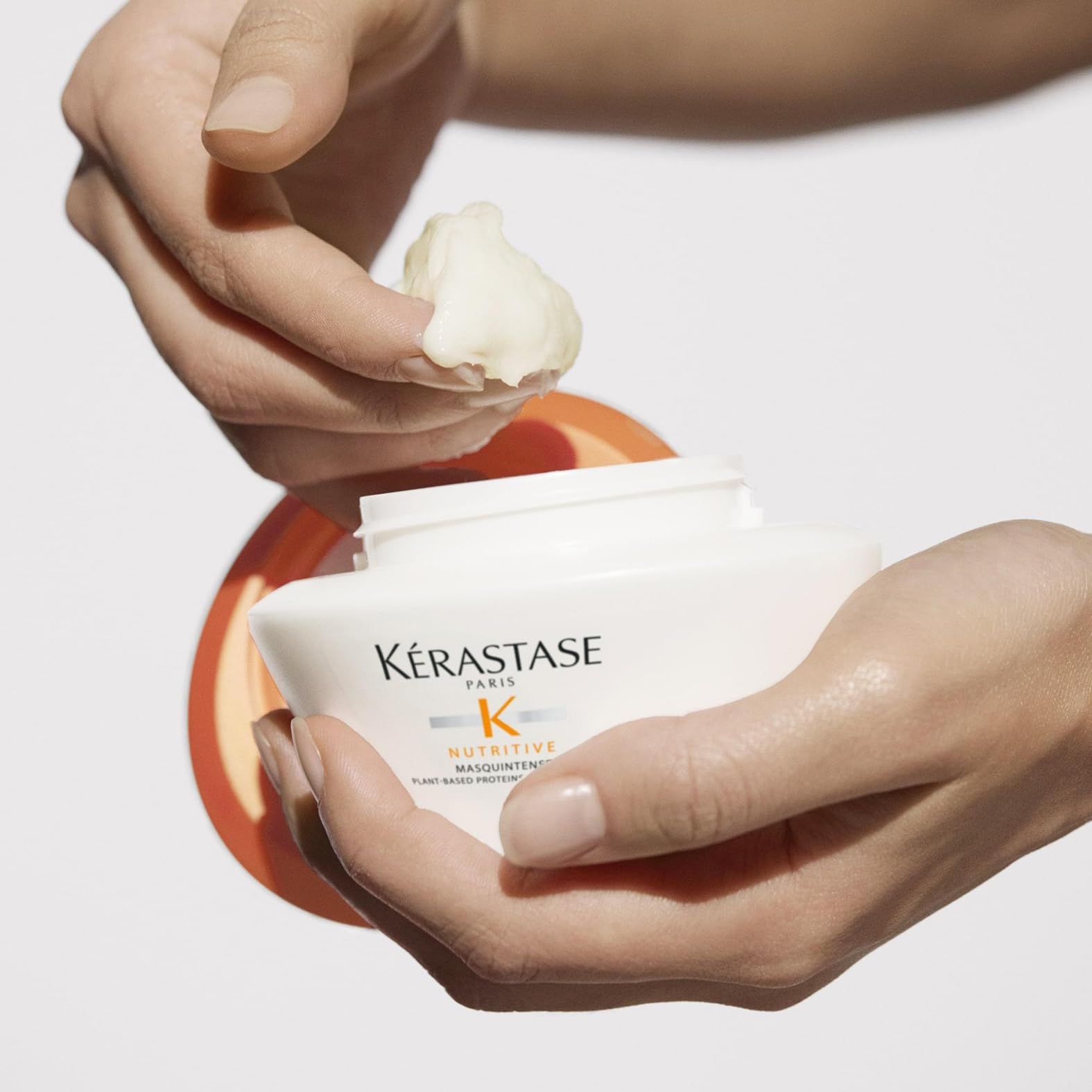 Hände nehmen eine kleine Menge Kérastase Nutritive Masquintense aus einem weißen Tiegel.