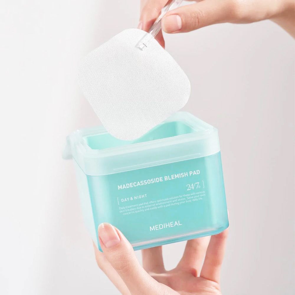Hände heben ein Pad aus einem türkisfarbenen Behälter mit "MADECCASSOSIDE BLEMISH PAD"-Aufschrift. Marke: MEDIHEAL.