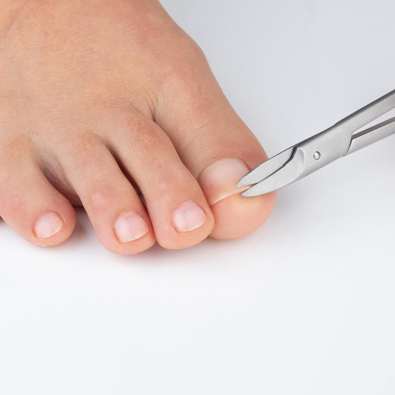 Nahaufnahme einer Person, die mit einer Fußnagelschere einen Zehennagel schneidet. Helle Umgebung. Produkt: remos.