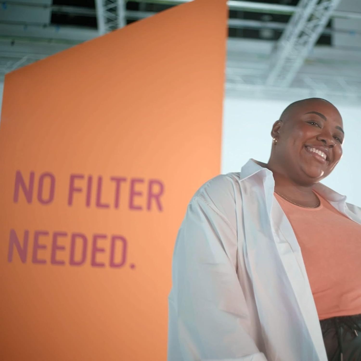 Frau vor orangefarbener Wand mit Text: NO FILTER NEEDED.
