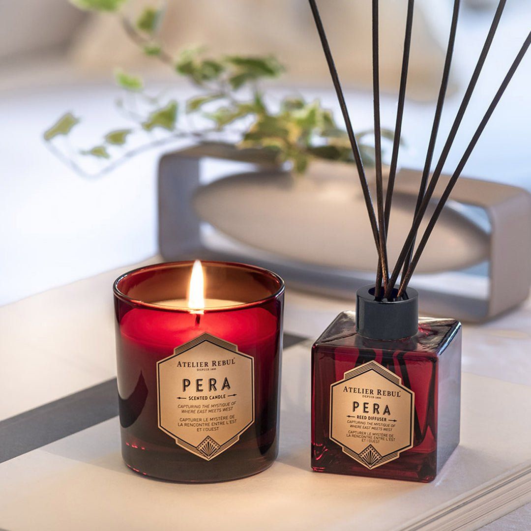 Rote Kerze und Diffusor mit schwarzen Stäbchen. Beide mit Etikett "Pera" von Atelier Rebul. Kerze brennt.