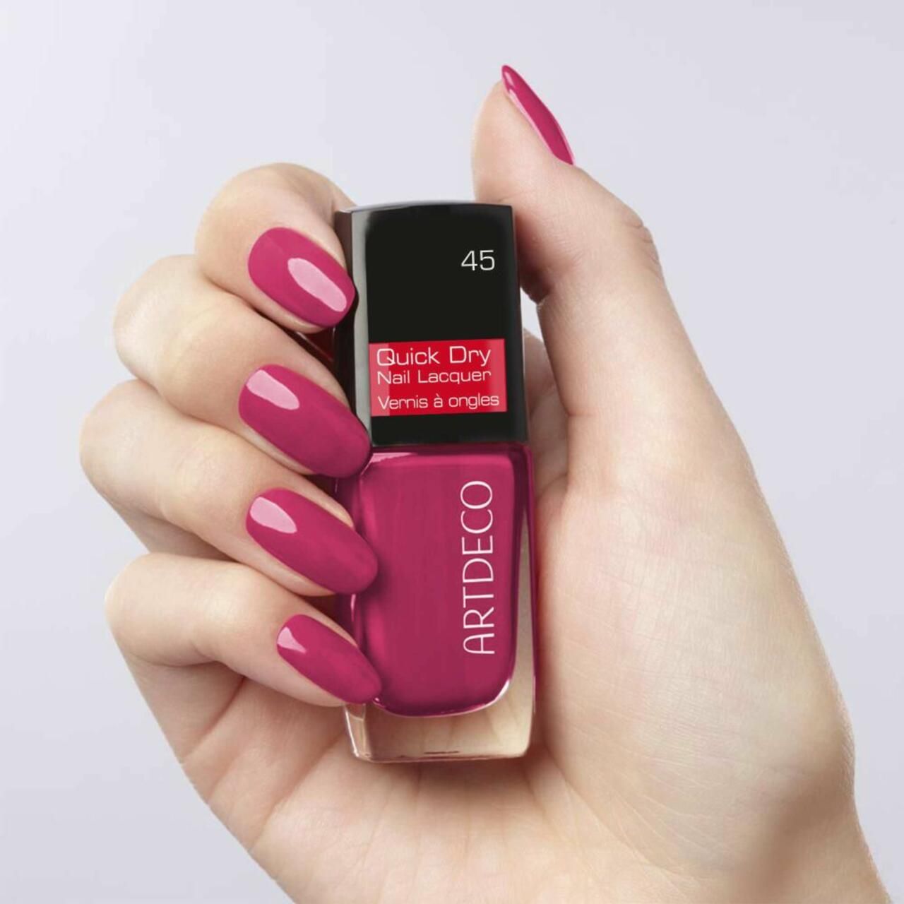 Hand hält Nagellackflasche. Lackierte Fingernägel in Rot. Marke Artdeco. Farbnummer 45.