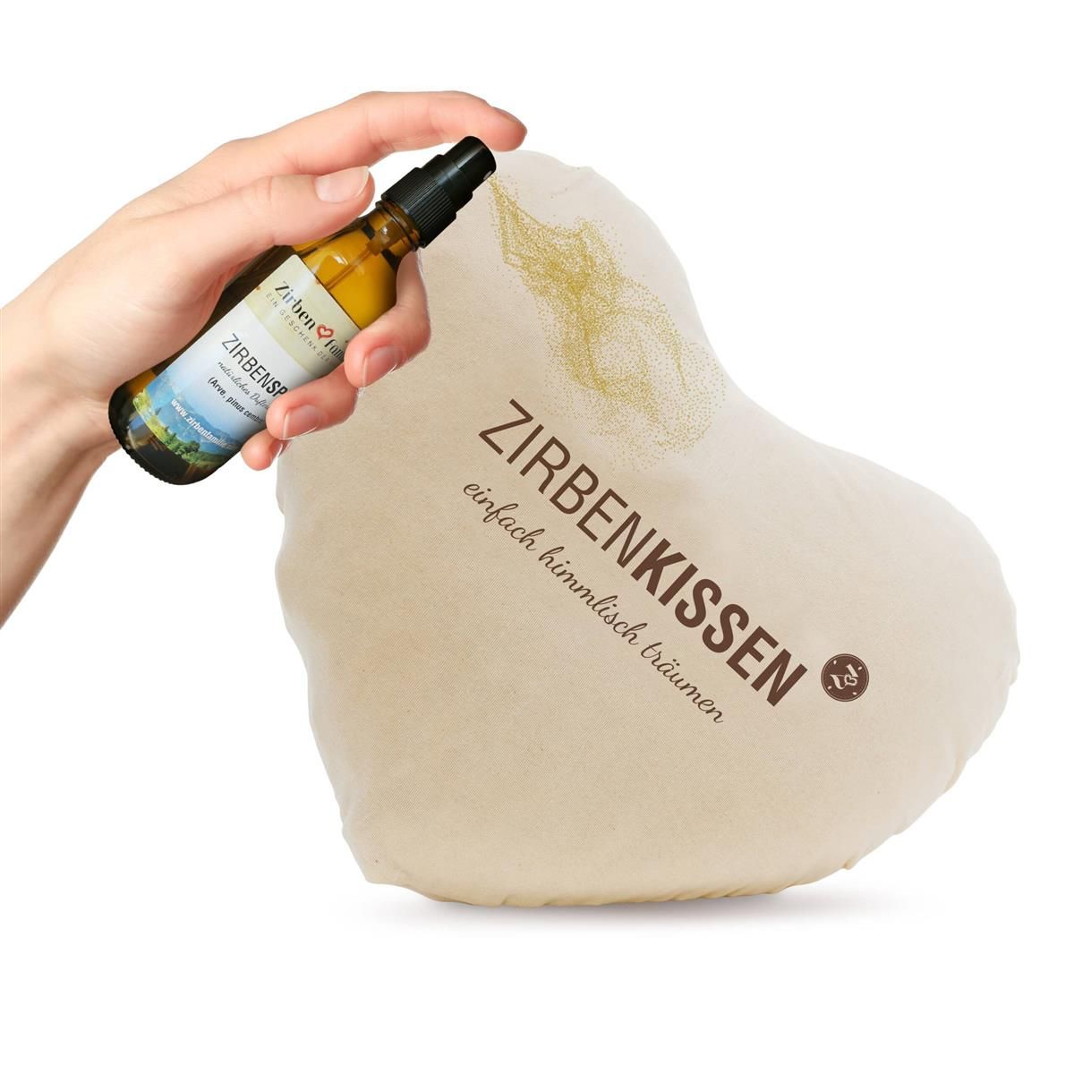 Herzförmiges, beiges Kissen. Text: Zirbenkissen. Eine Hand sprüht Spray auf das Kissen. Aufschrift: einfach himmlisch träumen.