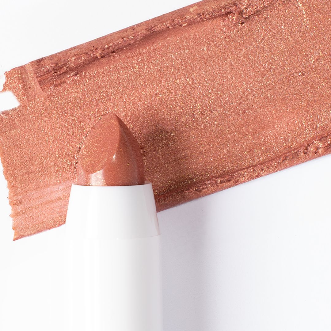 Nahaufnahme eines schimmernden, kupferfarbenen Lippenstifts und eines Farbmusters auf weißem Hintergrund.