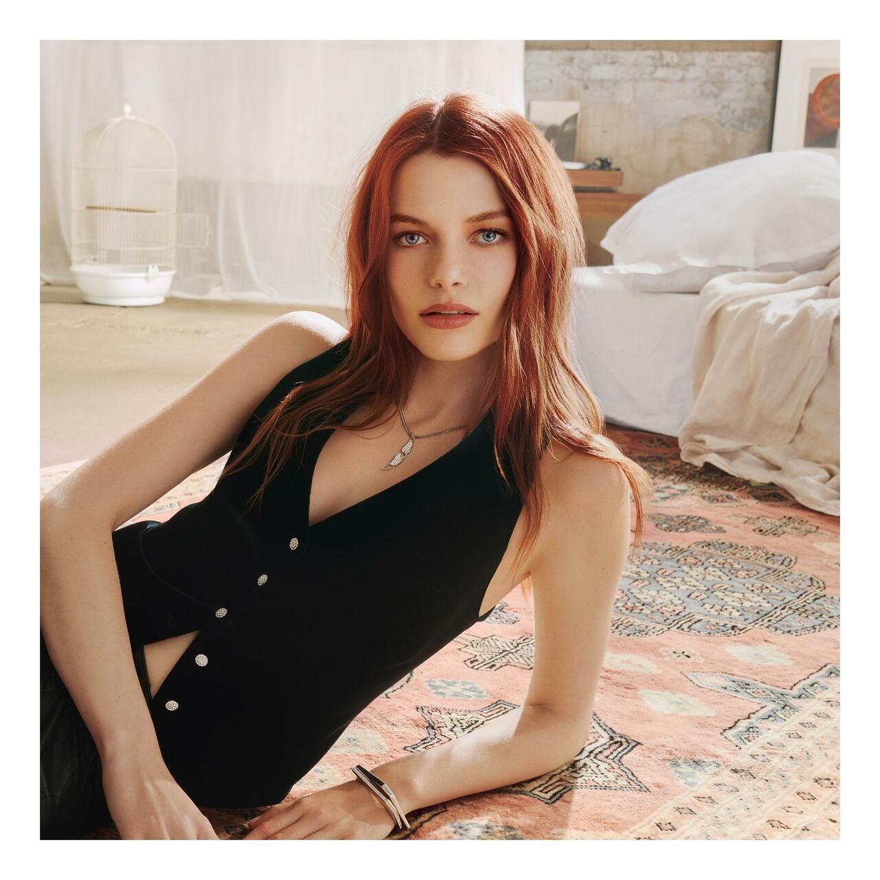 Frau mit roten Haaren liegt auf einem Teppich. Sie trägt eine schwarze Weste. Blick in die Kamera.