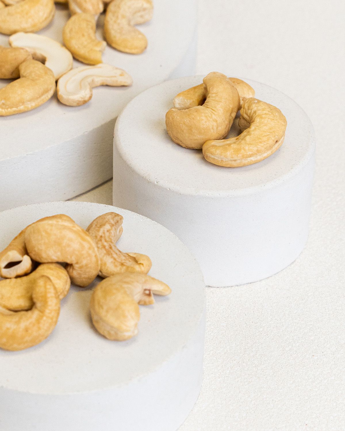 Cashewkerne auf weißen Podesten. Einige Kerne liegen lose daneben.