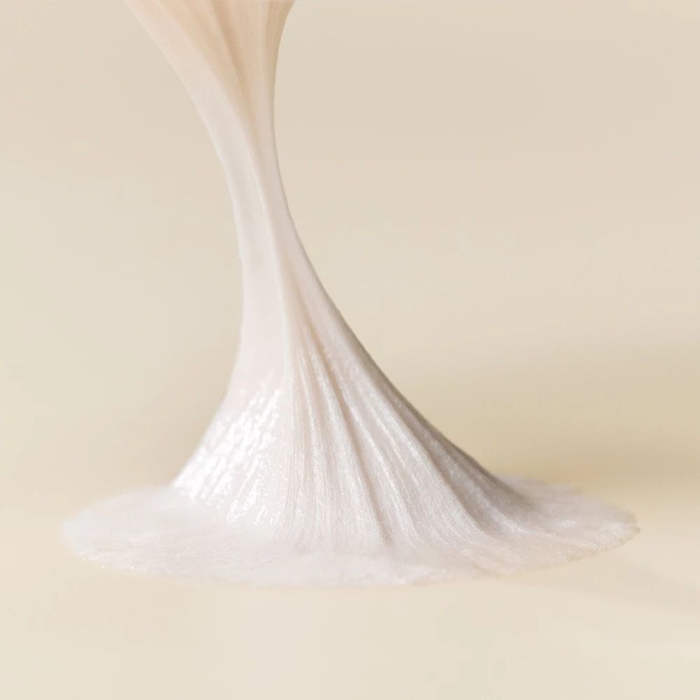 Nahaufnahme eines Strangs weißen Reinigungsschaums, der sich auf einer Oberfläche ausbreitet. Der Schaum hat eine glatte Textur.