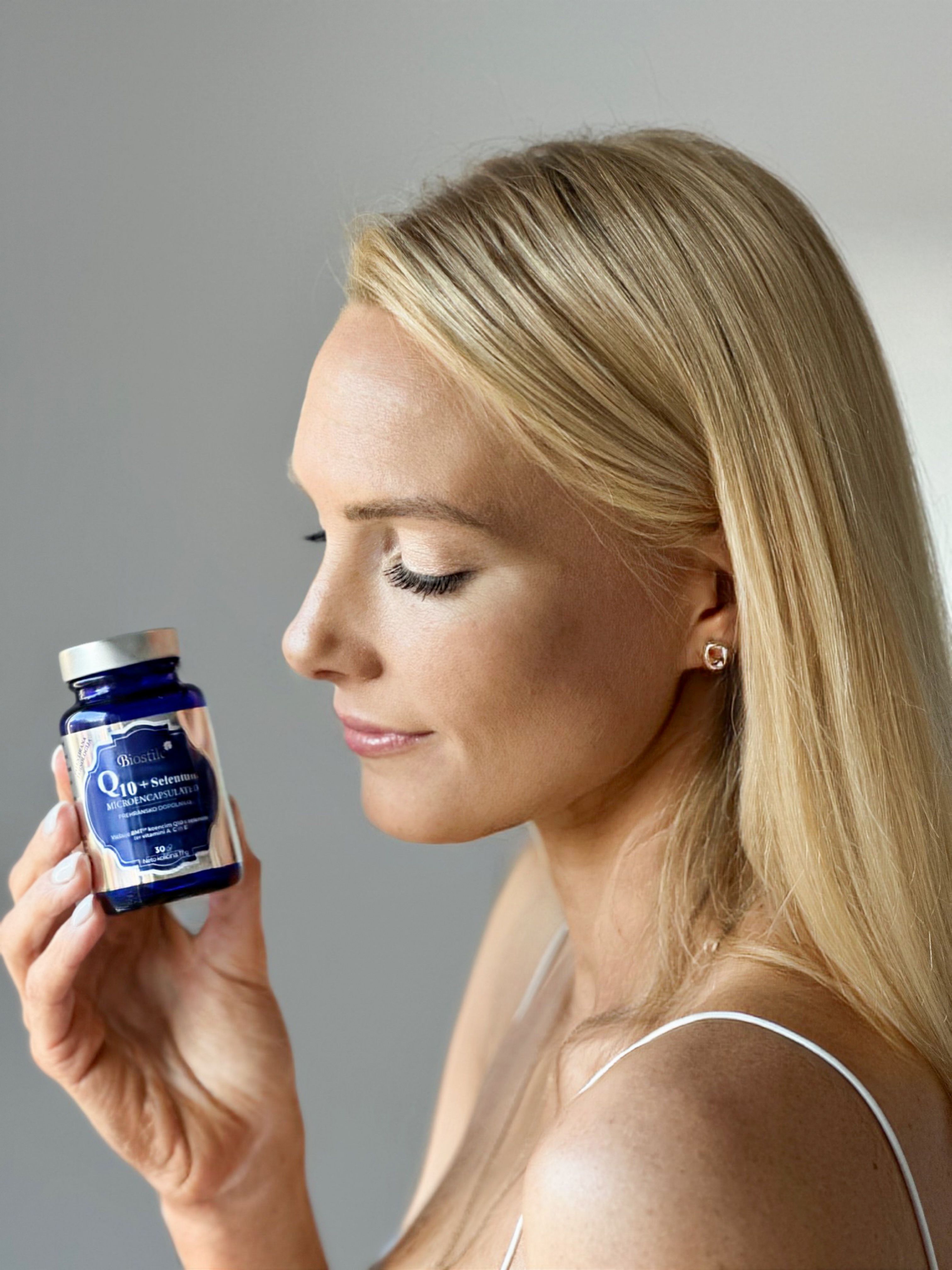 Frau hält eine blaue Flasche. Aufschrift: Q10+Selenium Microencapsulated. Flasche hat silbernen Verschluss.