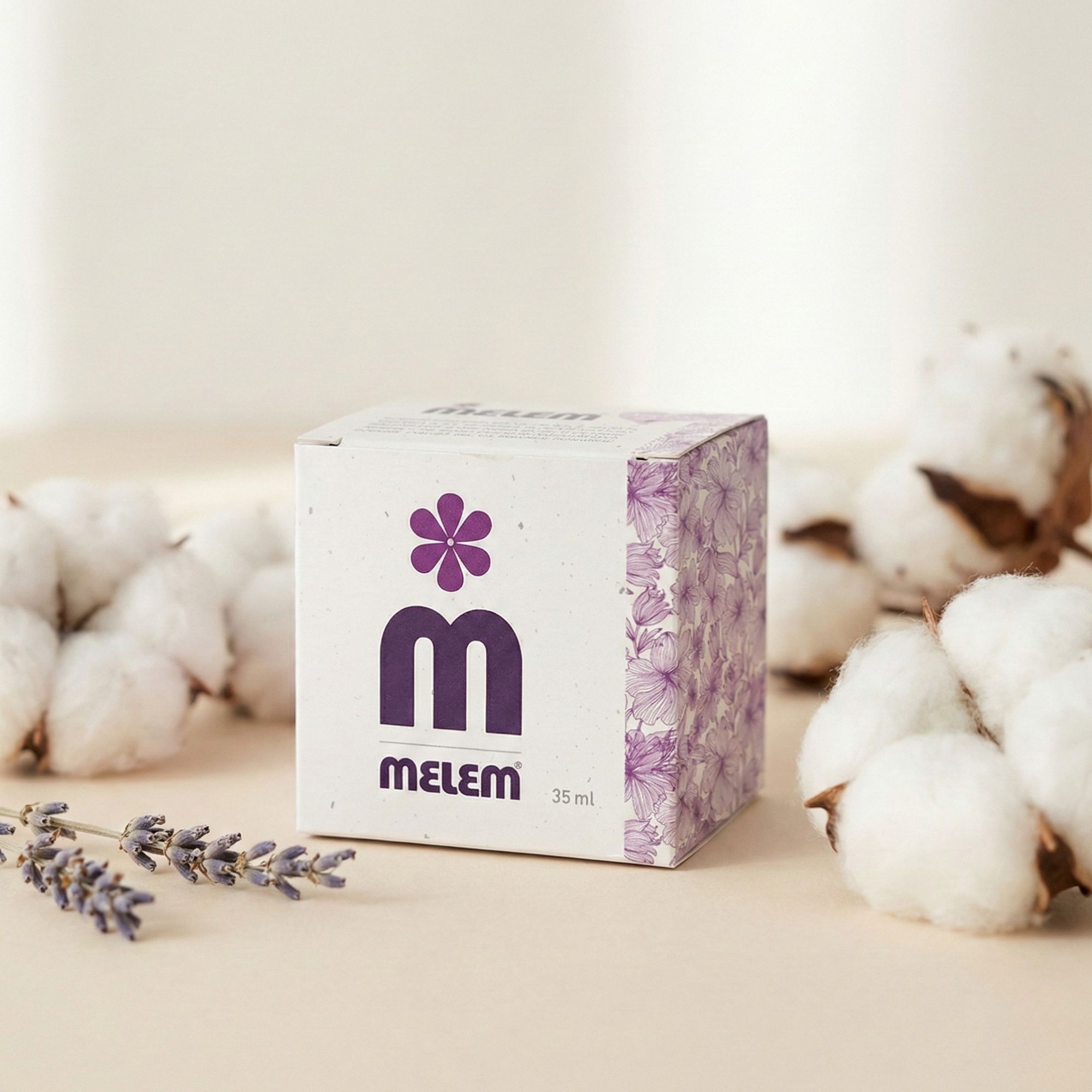 Verpackung mit lila Blumenmuster und Logo, umgeben von Baumwollblüten und Lavendel. Aufschrift: Melem, 35 ml.