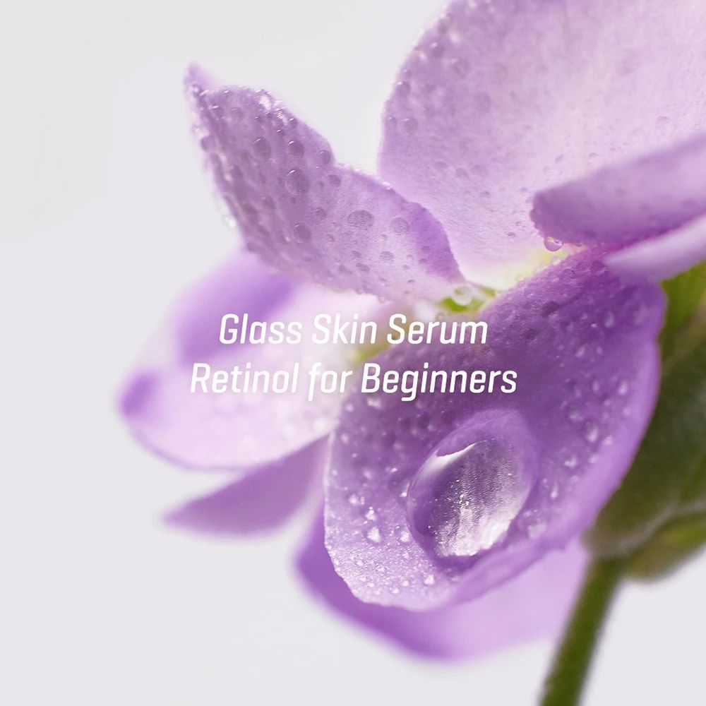 Nahaufnahme einer lila Blume mit Wassertropfen. Text: Glass Skin Serum Retinol for Beginners.