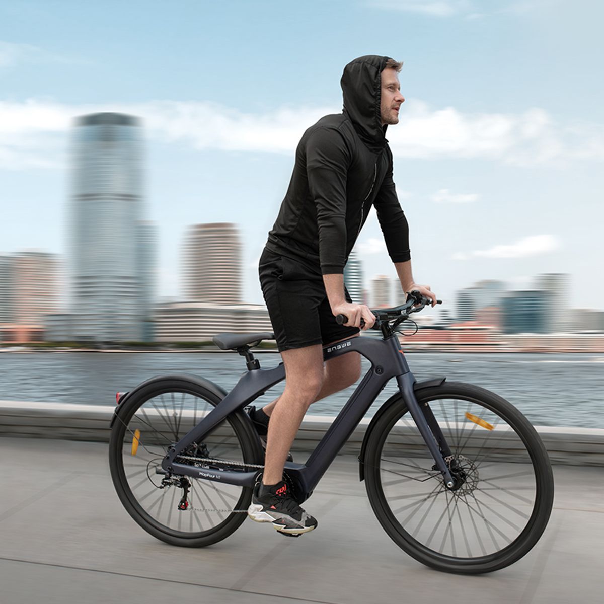 Person fährt auf einem dunkelgrauen Elektrofahrrad. Stadtlandschaft im Hintergrund. Engwe-Logo.