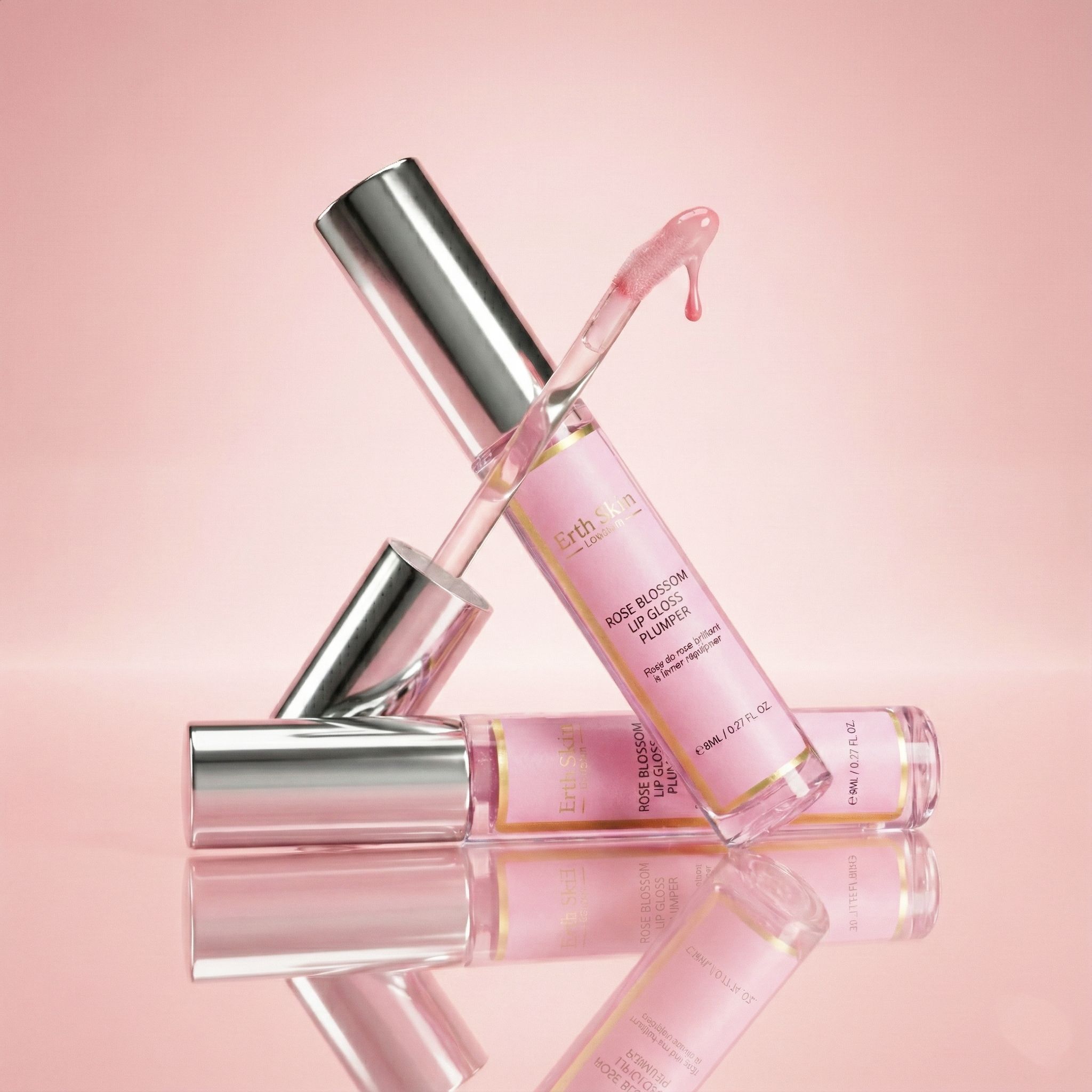 Zwei Lipglosse mit silbernen Kappen. Rosa Flüssigkeit. Ein Gloss liegt, einer steht. Rosa Hintergrund.