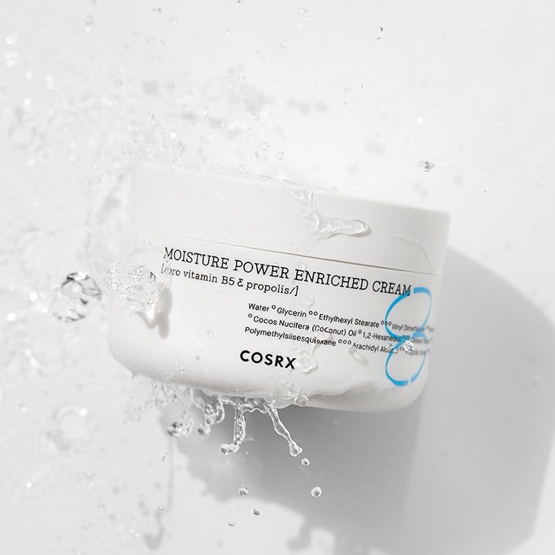 Weiße Creme-Dose mit Wasser. Aufschrift: MOISTURE POWER ENRICHED CREAM, COSRX. Wasser spritzt.