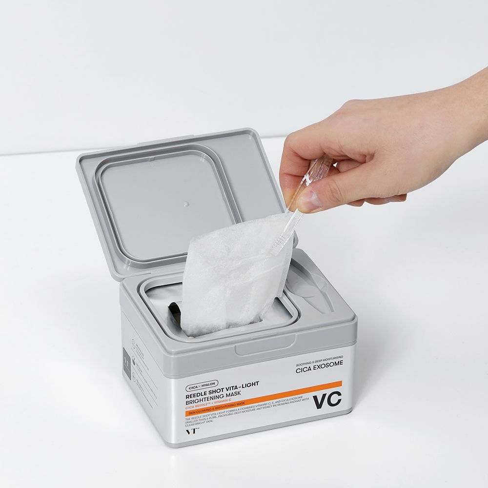 Hand entnimmt Maske aus grauer Box. Aufschrift: Reedle Shot Vita-Light Brightening Mask. Marke: VT. Offene Verpackung.
