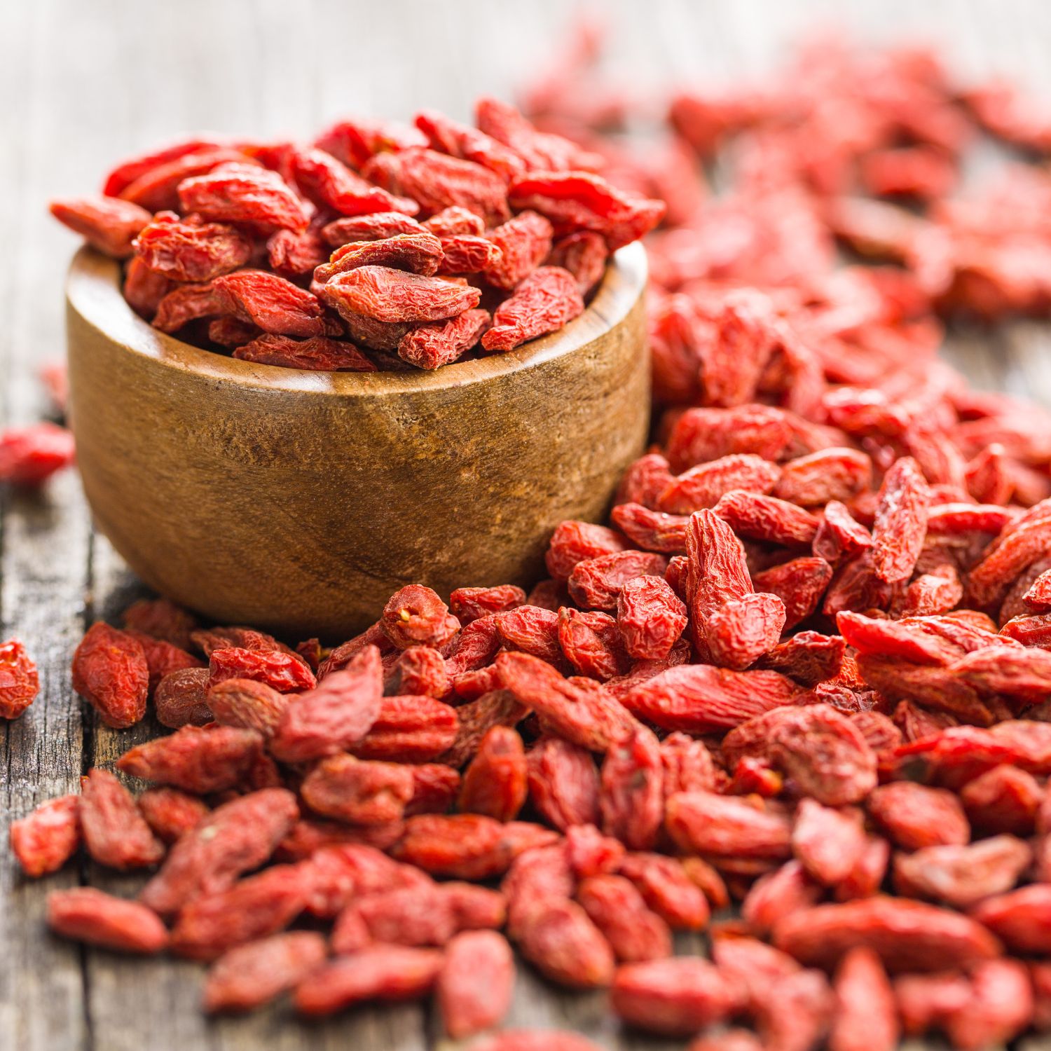Goji-Beeren in einer kleinen Holzschale und verstreut auf Holz. Rote Farbe, längliche Form.