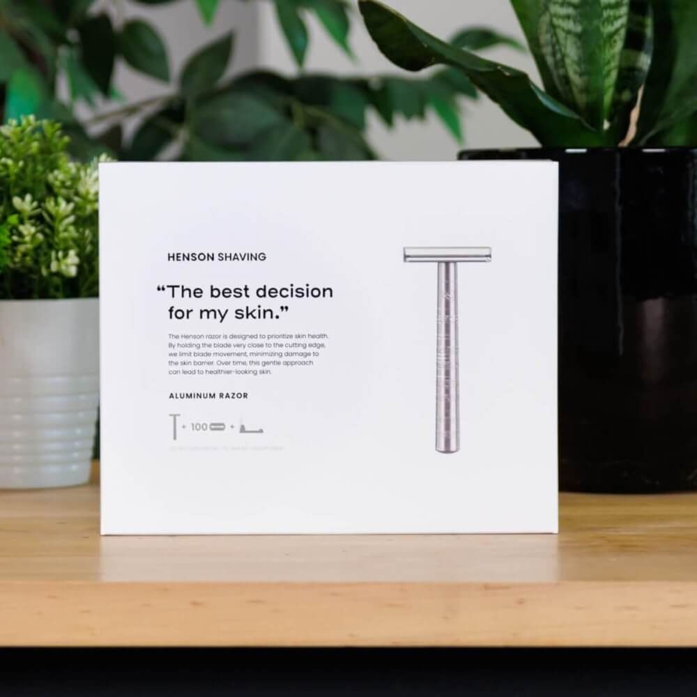 Weiße Verpackung mit Rasierer-Illustration. Text: HENSON SHAVING, "The best decision for my skin.", ALUMINUM RAZOR.