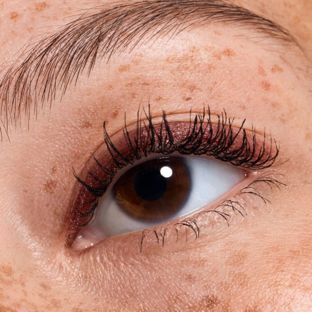 Nahaufnahme eines Auges mit rotem Lidschatten und Wimperntusche. Braune Iris.