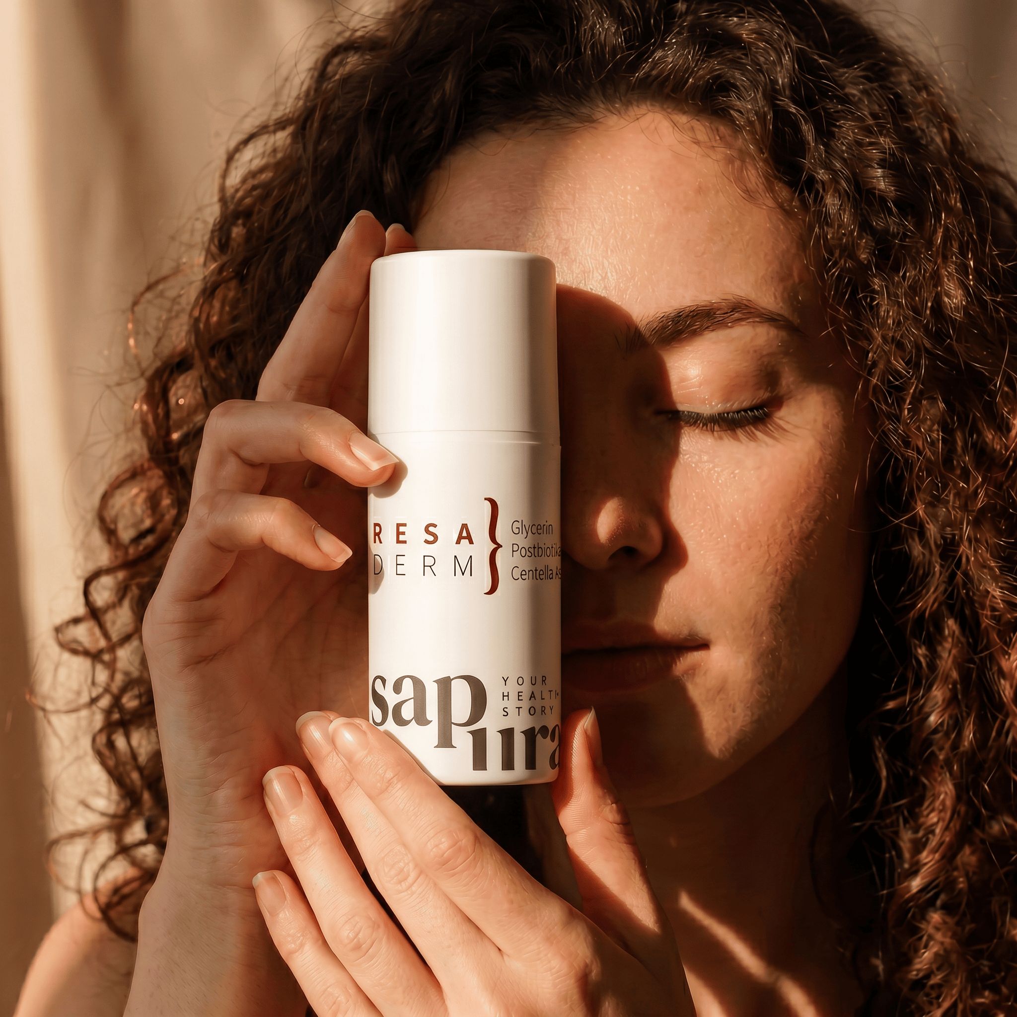 Frau hält weiße Pumpflasche mit Rosacea Creme vor ihr Gesicht. Produkt enthält Glycerin, Postbiotika, Centella Asiatica.