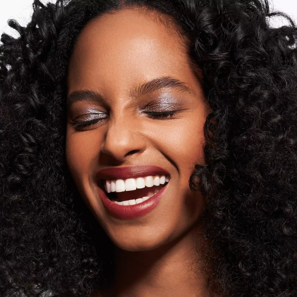 Frau mit Locken, geschlossenen Augen, Lidschatten. Lippenstift. Lächelt. Helle Haut.