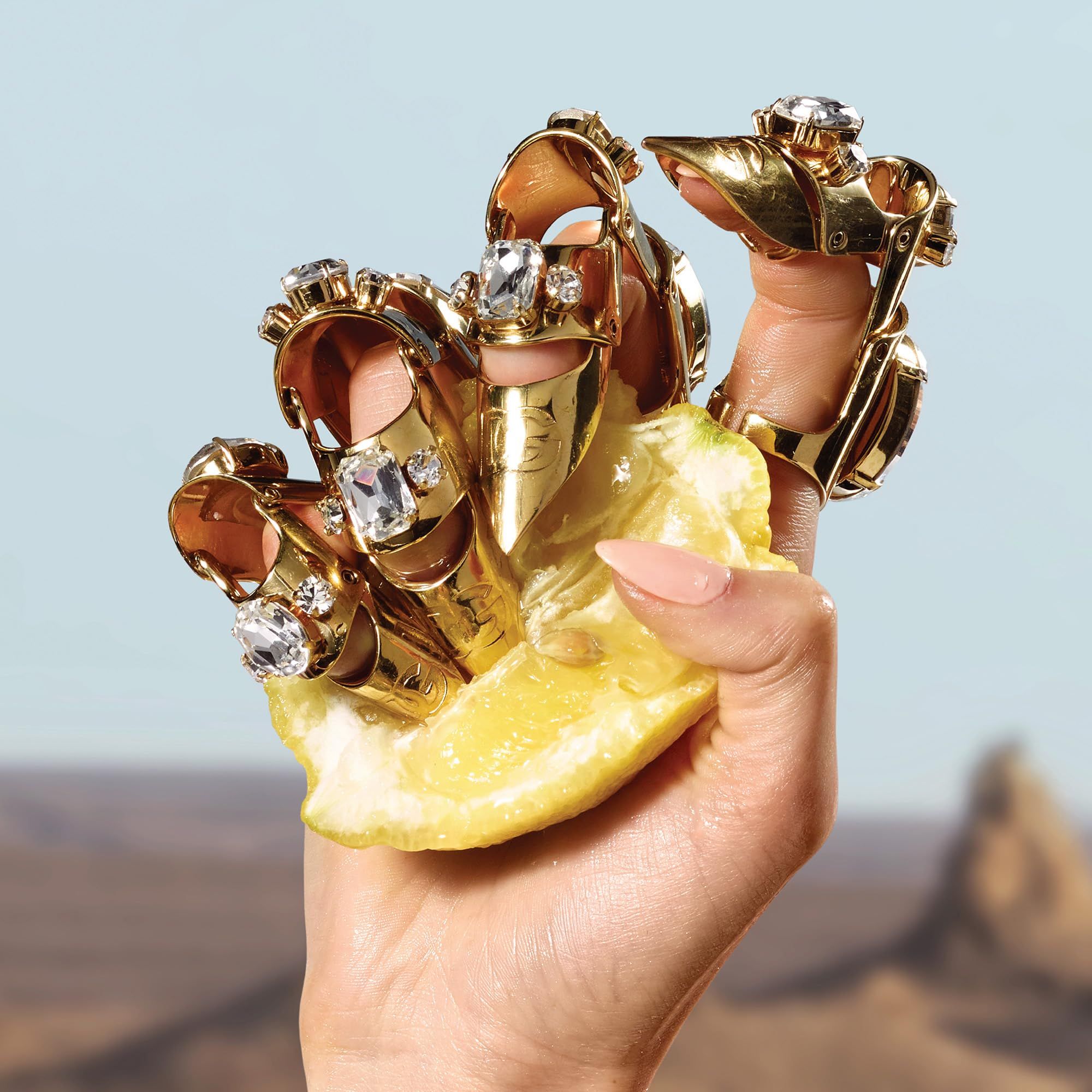 Hand hält Zitrone mit goldenen Ringen mit Diamanten. Hintergrund: Landschaft mit blauem Himmel.
