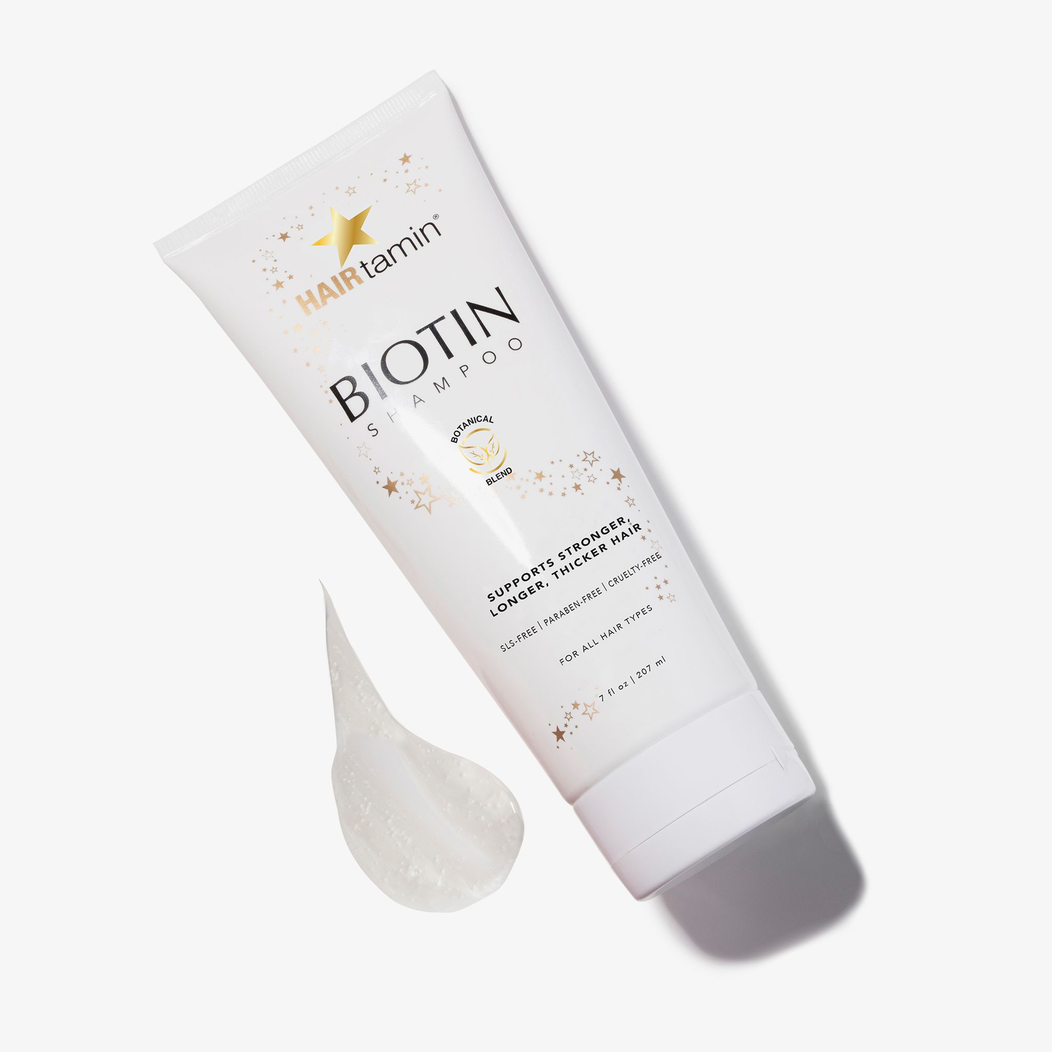 Weiße Tube "HAIRtamin Biotin Shampoo" mit Auslauf. Sterne und Schriftzug "Botanical Blend". Text: "Supports stronger, longer, thicker hair".