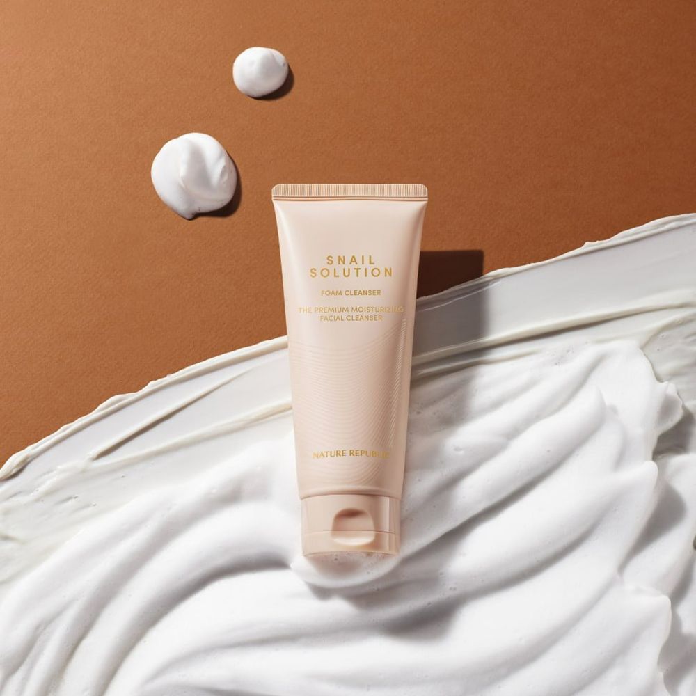Beige Tube mit "Snail Solution Foam Cleanser" und Schaum. Text: "The Premium Moisturizing Facial Cleanser". Marke: NATURE REPUBLIC.