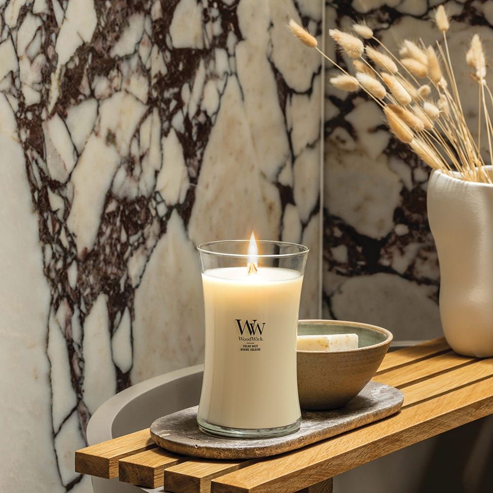 Kerze mit Flamme. WoodWick-Logo. Auf einem Holztablett, neben einer Schale. Hintergrund: Marmor.