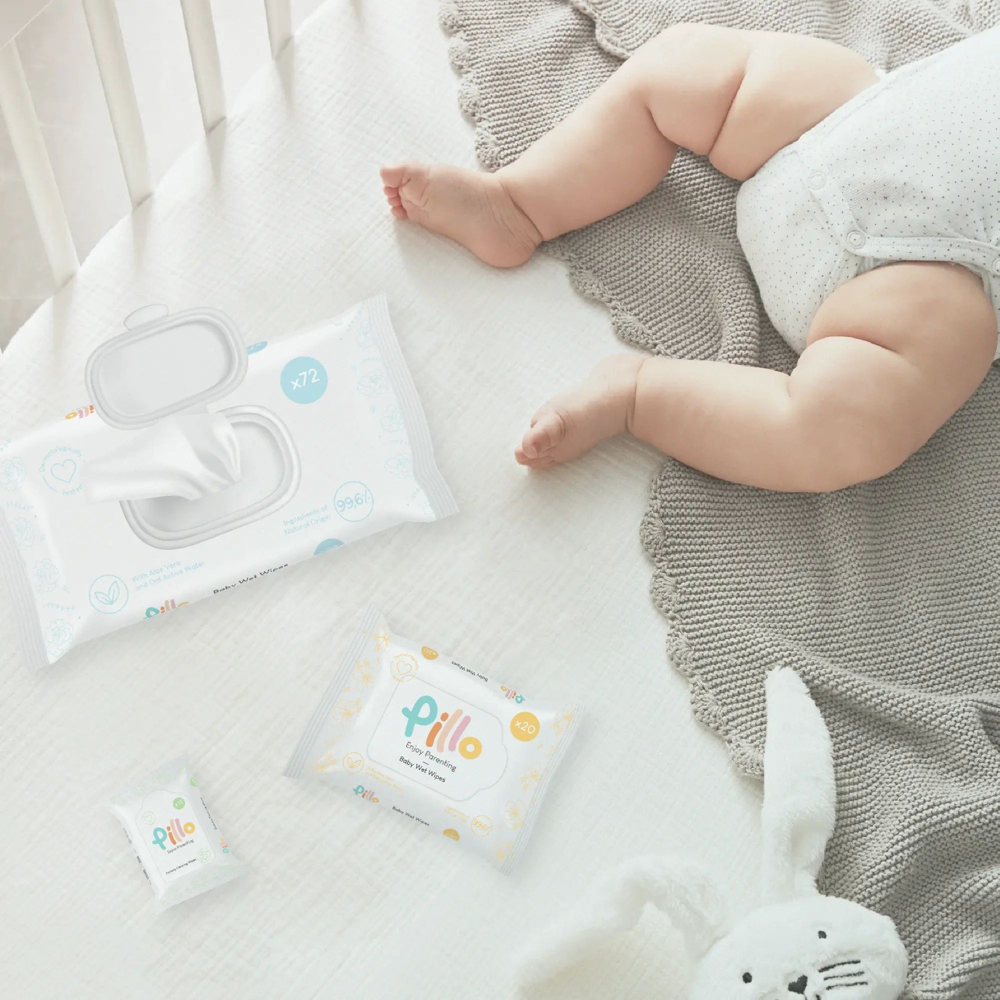 Pillo Baby Feuchttücher. Mehrere Packungen, darunter eine geöffnete, liegen auf einer weißen Oberfläche. Ein Baby liegt daneben.