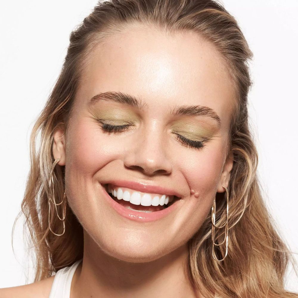 Nahaufnahme einer lächelnden Frau mit Make-up und goldenen Ohrringen.