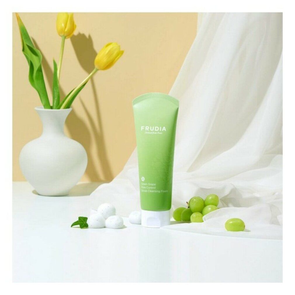 Grüne Tube mit weißem Verschluss. Aufschrift: FRUDIA. Text: Green Grape Pore Control Scrub Cleansing Foam. Neben Trauben und Vase.