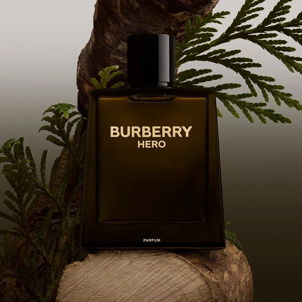 Braune Parfümflasche mit schwarzem Deckel. Aufschrift: Burberry Hero. Dekoration mit Holz und Grün.